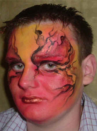 Face Painting: Adult male with full face painted in blended shades of red, orange, yellow and black providing a flaming effect.