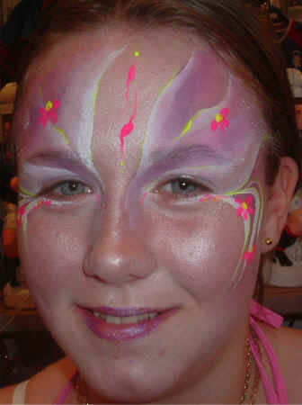 Face Painting: Adult female with pink and white princess face highlighted with orange and yellow flowers.